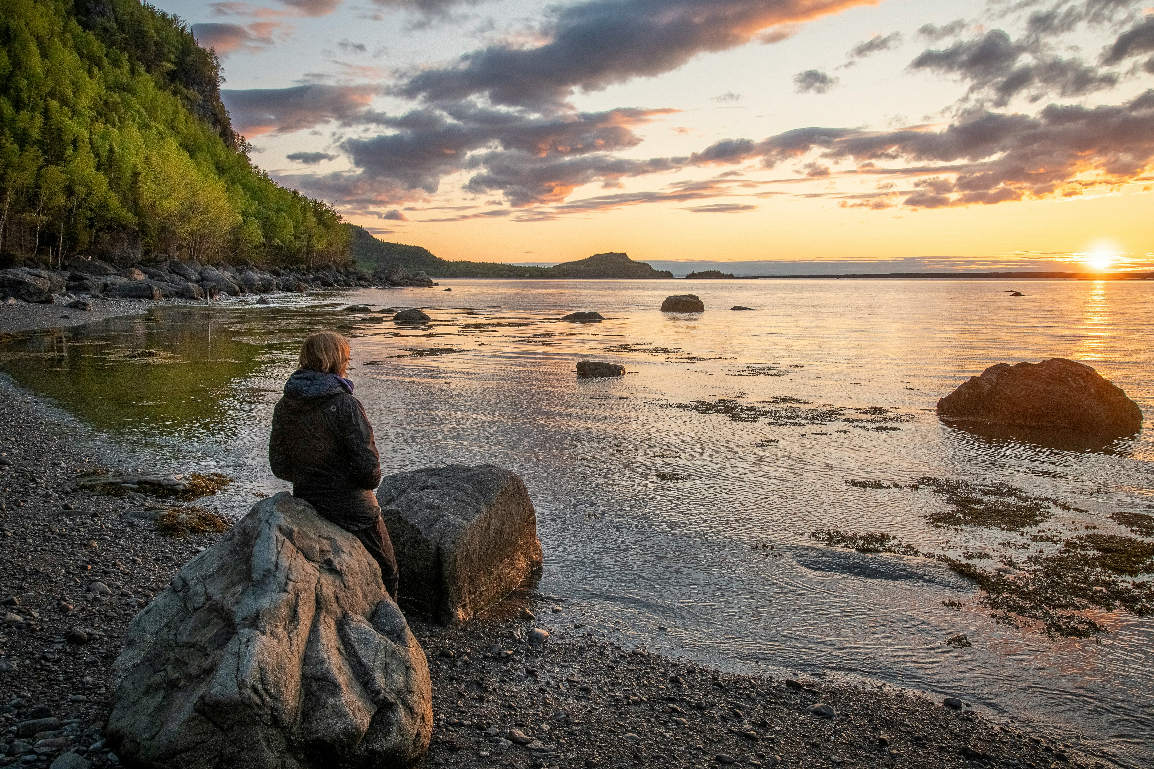 woman in black jacket sitting on rock by the sea during daytime